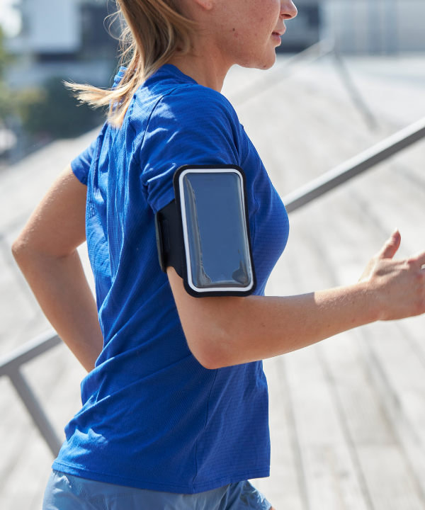 Une femme courant en extérieur, portant un brassard de sport magnétique Shapeheart avec pochette détachable, fixé sur son bras.